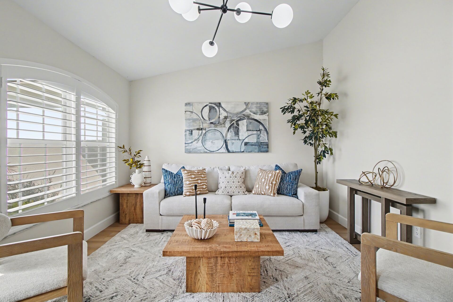 Staged living room with a large arched window, black sputnik chandelier, cream sofa and a wood block coffee table
