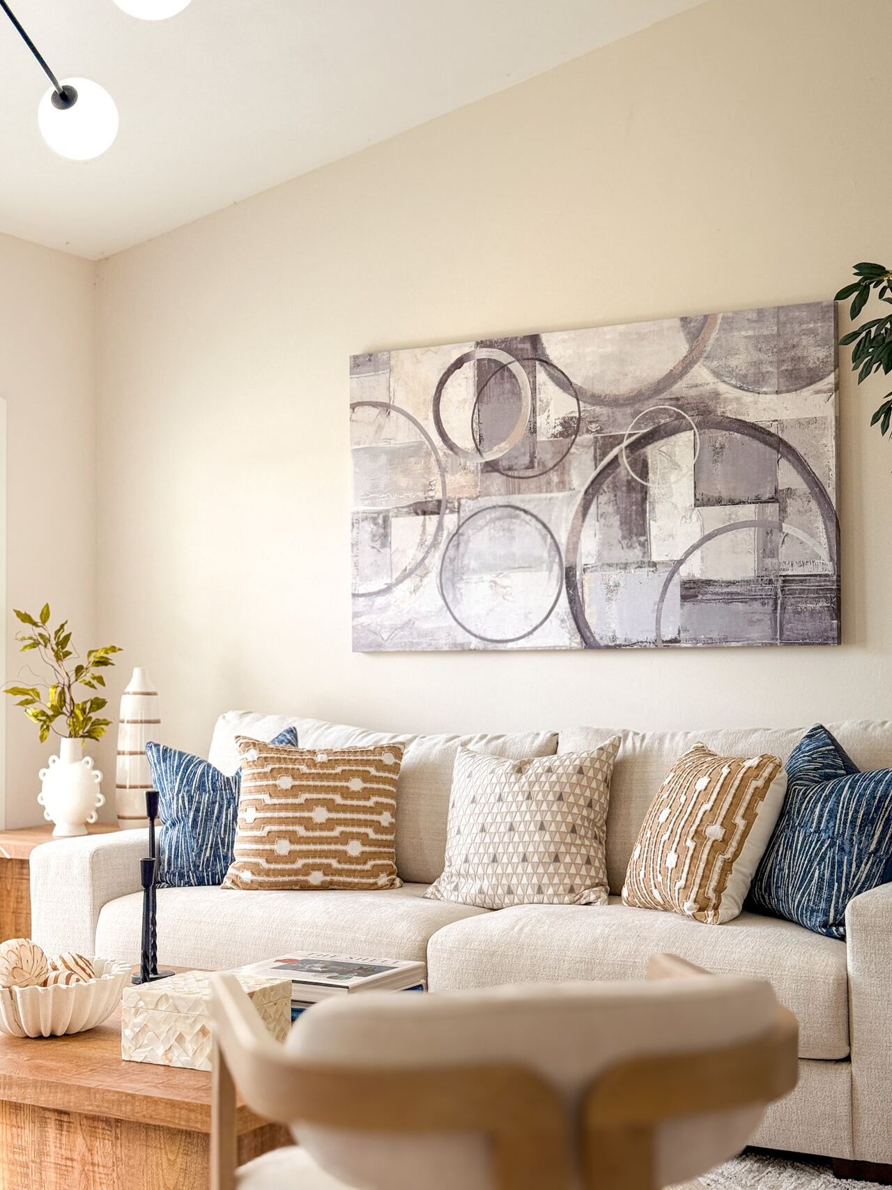Cream sofa layered with blue and tan patterned pillows beneath a circular abstract canvas